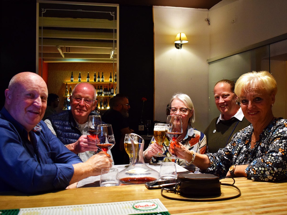 Five people sit at a bar table holding drinks, smiling at the camera.