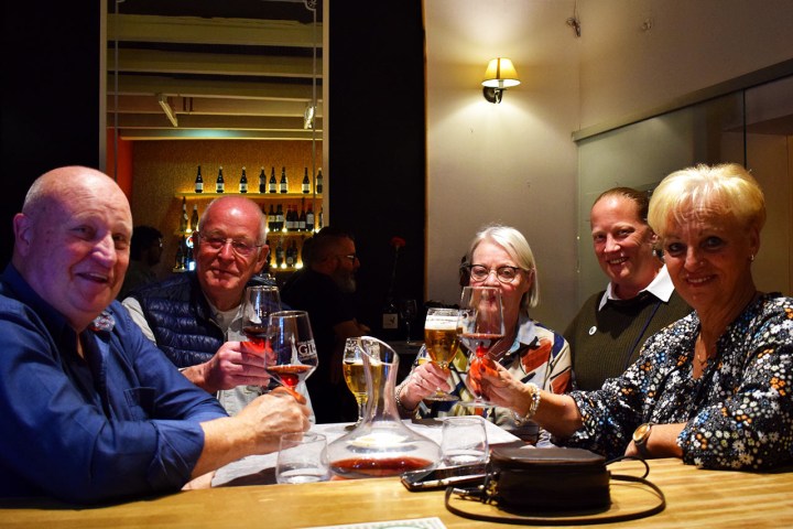 Five people sit at a bar table holding drinks, smiling at the camera.