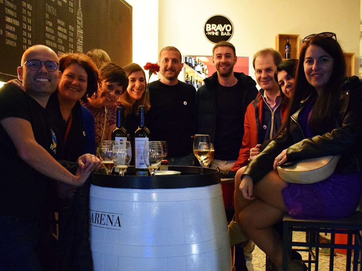 Group of people smiling around a wine barrel table in a wine bar.