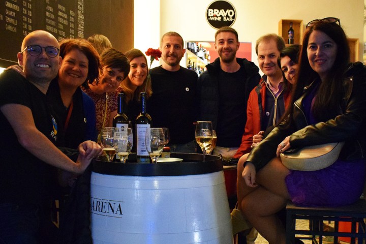 Group of people smiling around a wine barrel table in a wine bar.