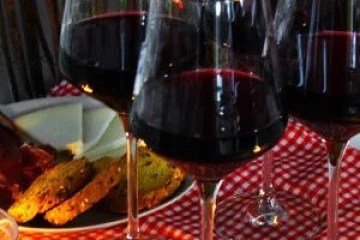 Four glasses of red wine on a checkered tablecloth with snacks.