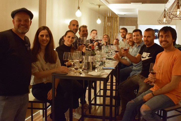 Group of people at a bar table with drinks, smiling at the camera.