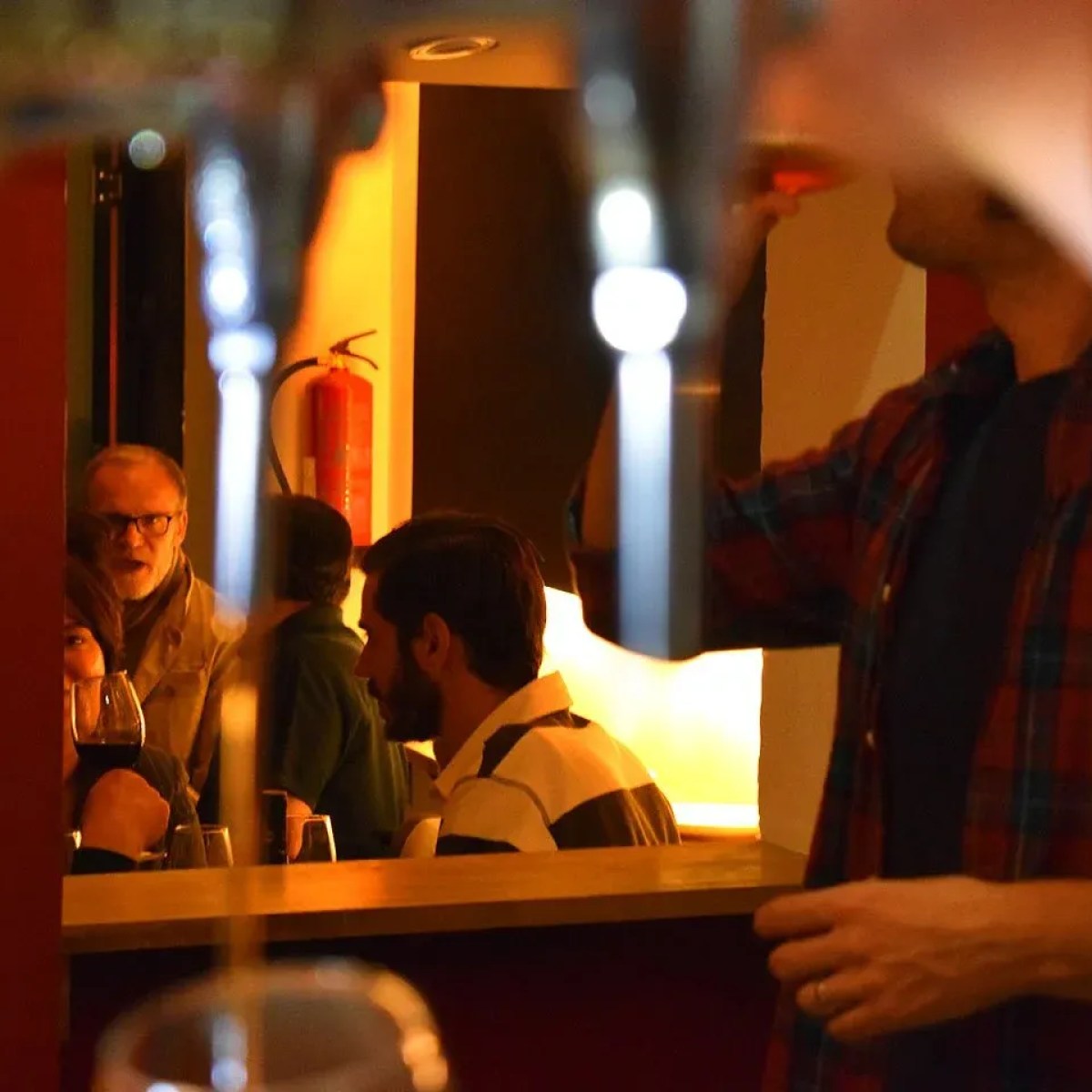 People sitting at a bar, one person drinking, warm lighting.