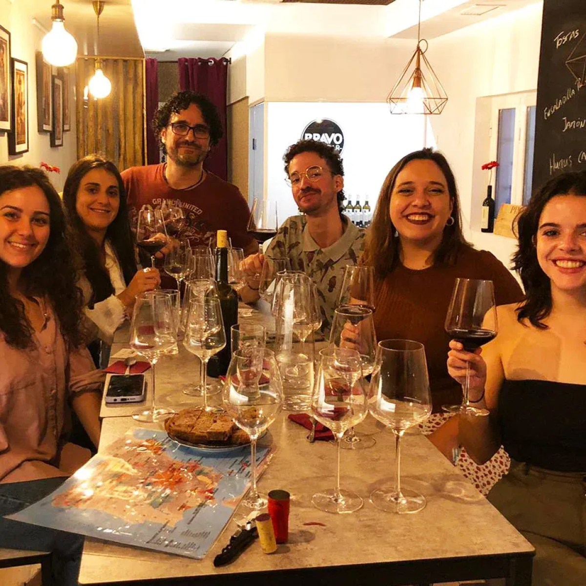 Group of six people smiling with wine glasses at a table indoors.
