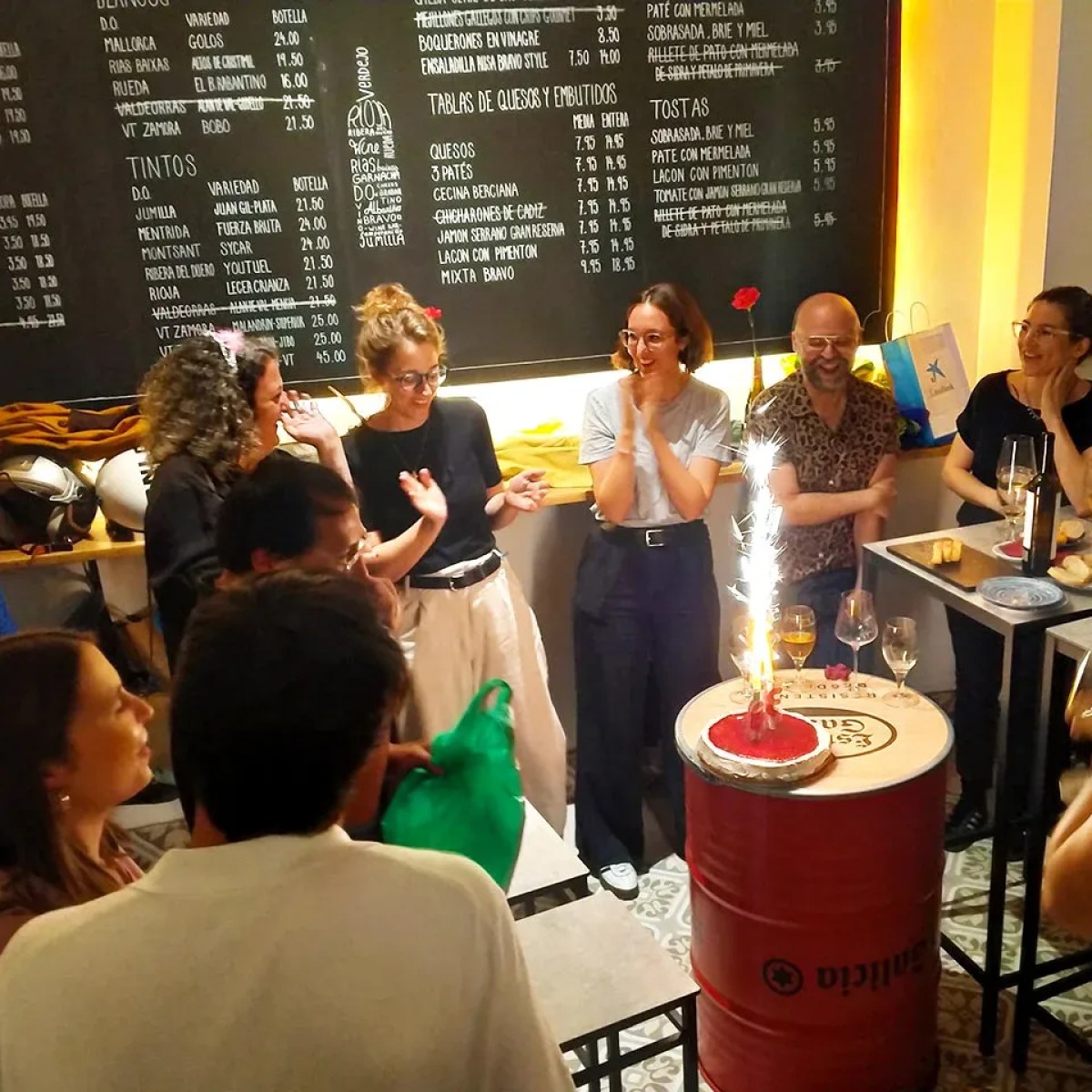 Group of people celebrating with a cake and sparkler at a restaurant.