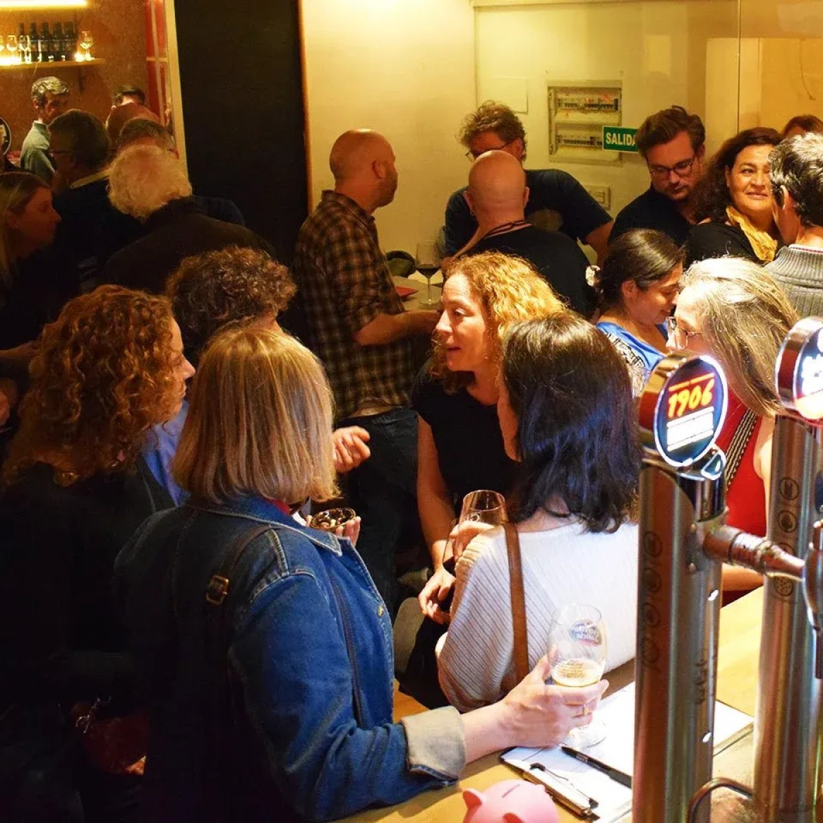 Crowded bar with people socializing and holding drinks.