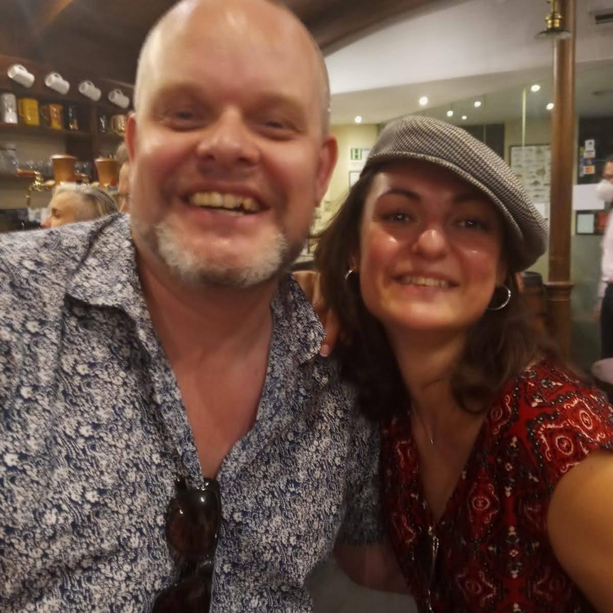 Smiling man and woman in a restaurant, woman wearing a flat cap.
