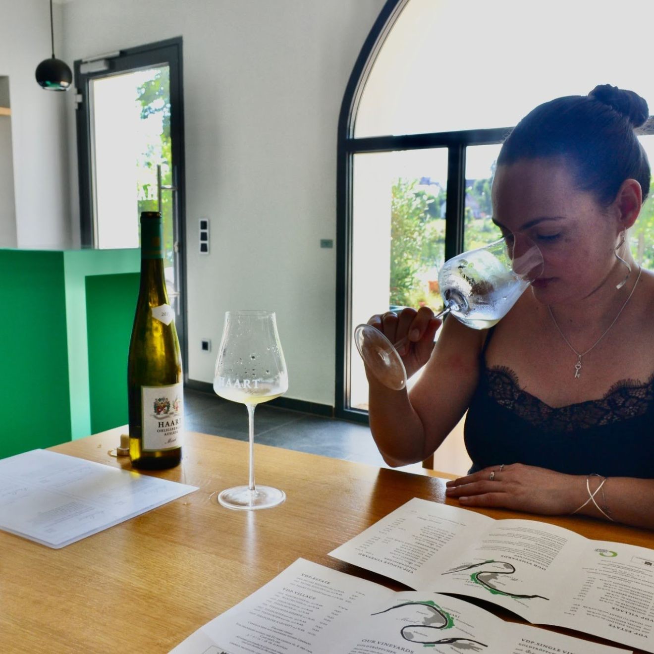 Woman tasting wine at a table with bottles and glasses.