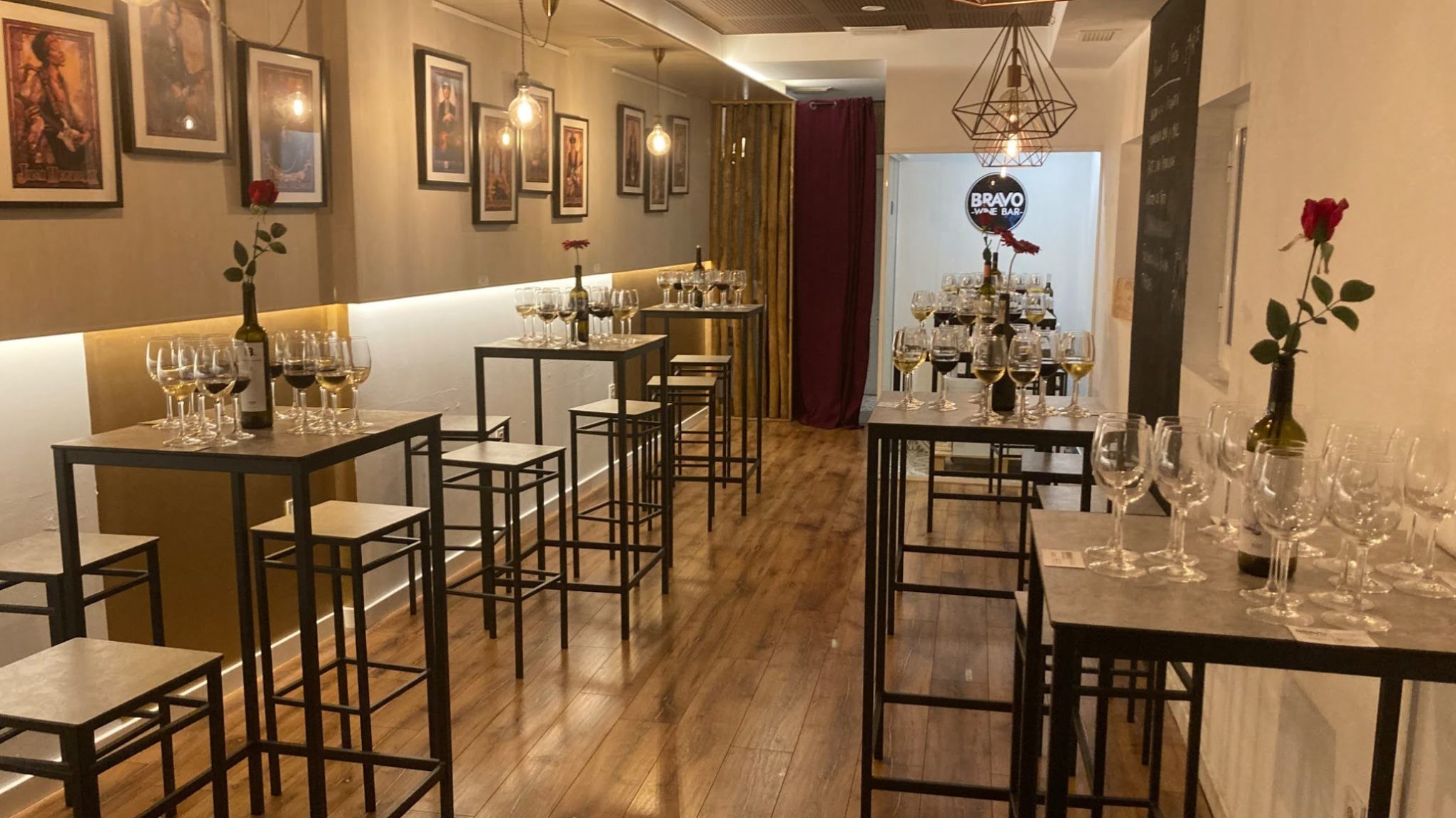 Cozy room with tall tables, chairs, wine glasses, framed art, and pendant lights.